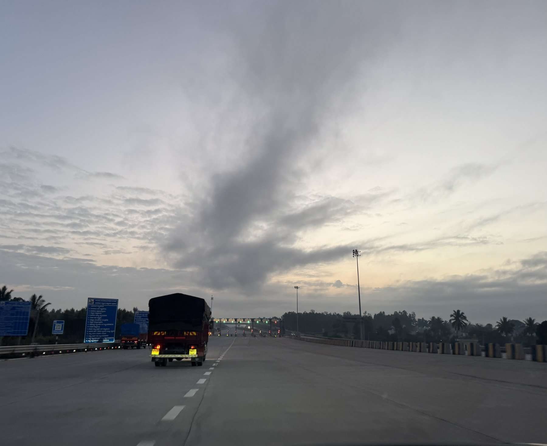 A highway on an Indian industrial corridor at dusk, a covered truck heading towards a toll plaza