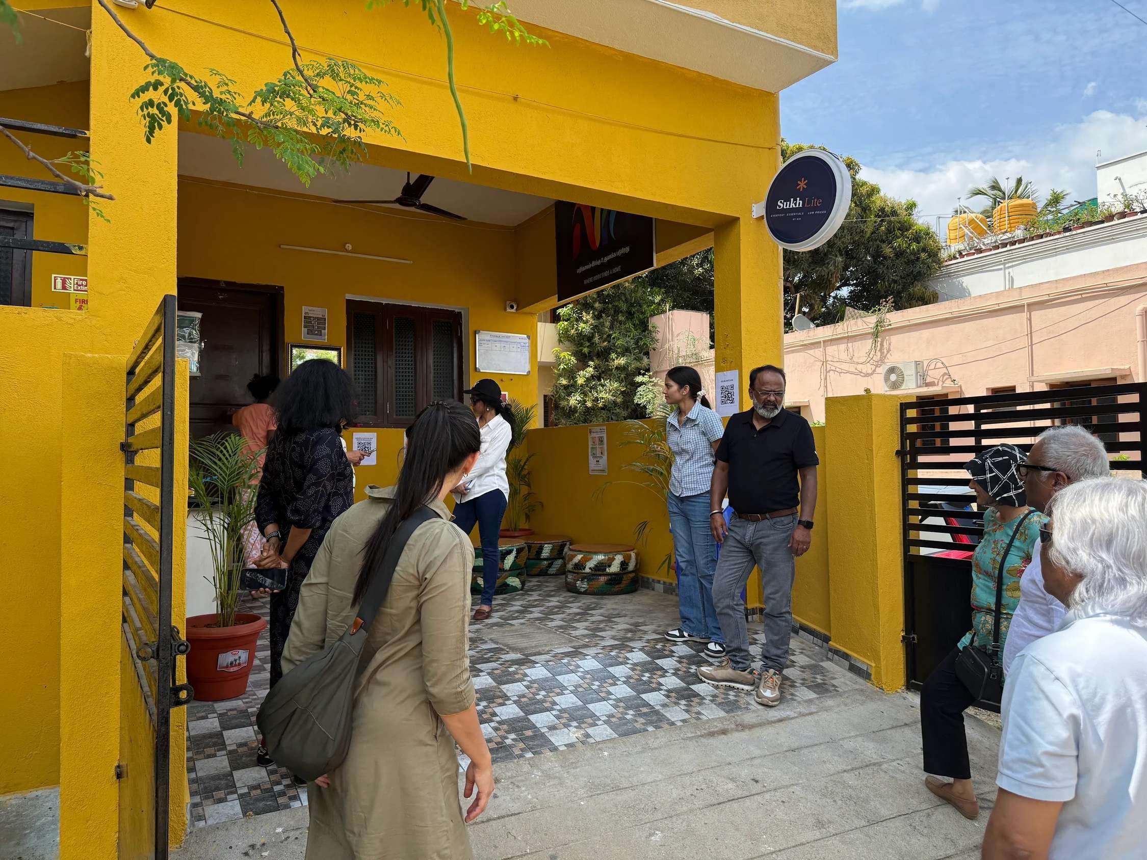 Visitors at the bright yellow entrance of a Nia Studio, with a Sukh Lite store sign and tyre seating